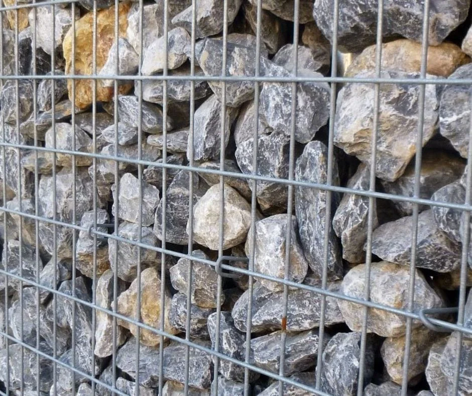 Tuinhout en blokhutten Close-up van een schanskorf schutting met een stevig metalen raster, gevuld met natuurstenen in grijstinten.