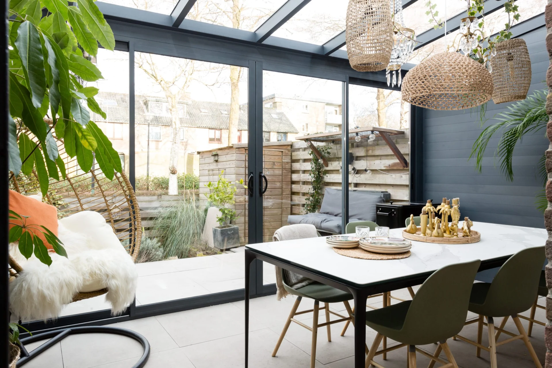 Tuinkamer Moderne Profiline tuinkamer met een grote antracietkleurige schuifpui, ingericht met een stijlvolle eethoek, hangstoel en sfeervolle verlichting, waardoor binnen en buiten naadloos in elkaar overlopen.