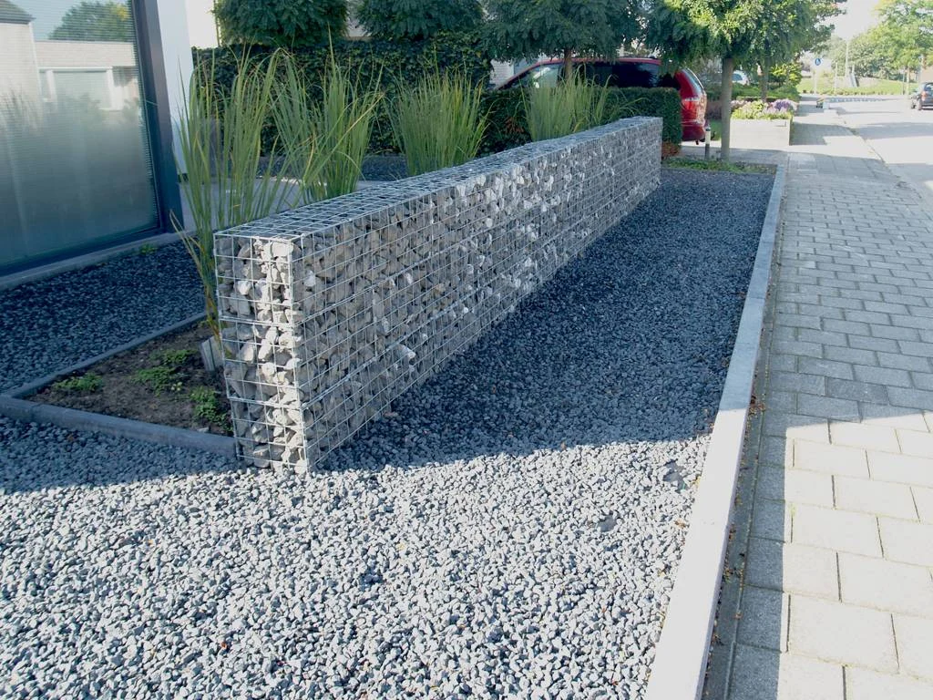 Tuinhout en blokhutten Schanskorf gevuld met natuursteen als moderne tuinafscheiding, omringd door grind en groenbeplanting.