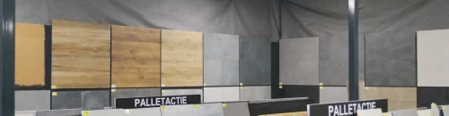 Een tegelshowroom met een grote selectie aan keramische tegels, waaronder houtlook, betonlook en marmerlook tegels. Op de voorgrond staan pallets met diverse aanbiedingen, aangegeven met het bord "Palletactie".