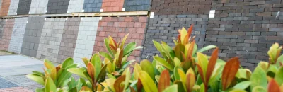 Een buitendisplay met verschillende soorten dakshingles in diverse kleuren en gebakken klinkers, geschikt voor daken, opritten en tuinbestrating.