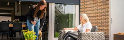 Donkergrijze screens gemonteerd op een bakstenen gevel, bieden effectieve zonwering en privacy voor een schuifpui met terras.